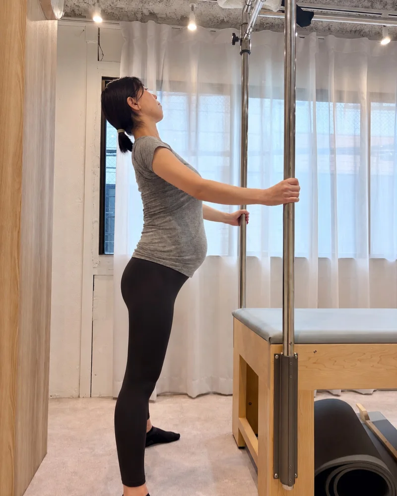 妊娠中の会員様が、キャデラックのポールを両手で持ち、胸を開くストレッチを行っている様子