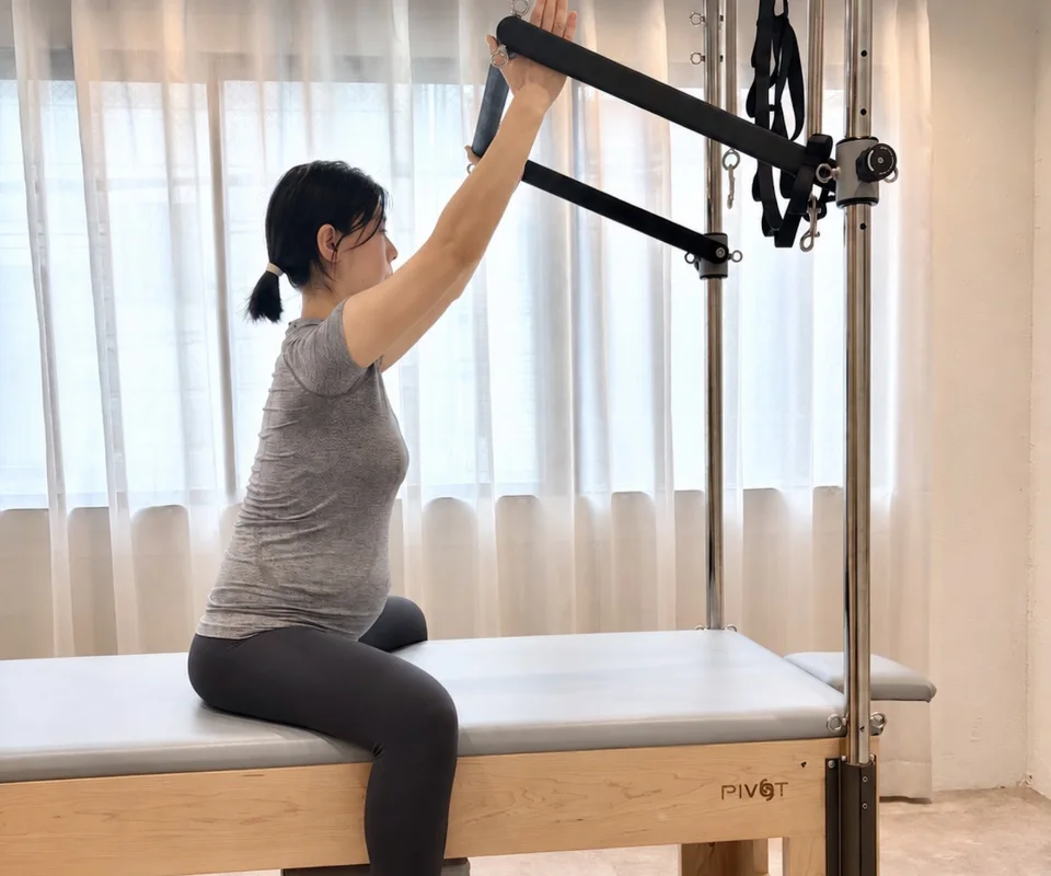 妊娠中のお客様が、キャデラックのバーを両手で押し上げるマタニティピラティスを行っている様子